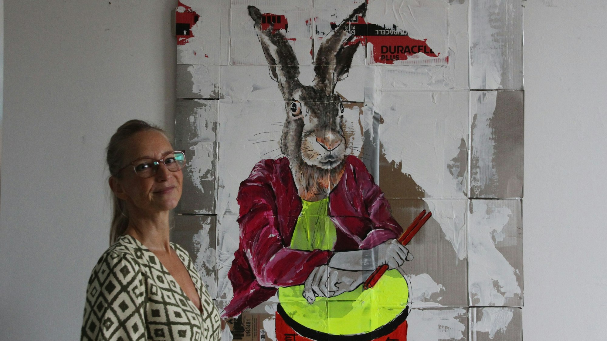 Eine Malerin vor einem Bild eines Hasen mit Trommel und Trommelstöcken