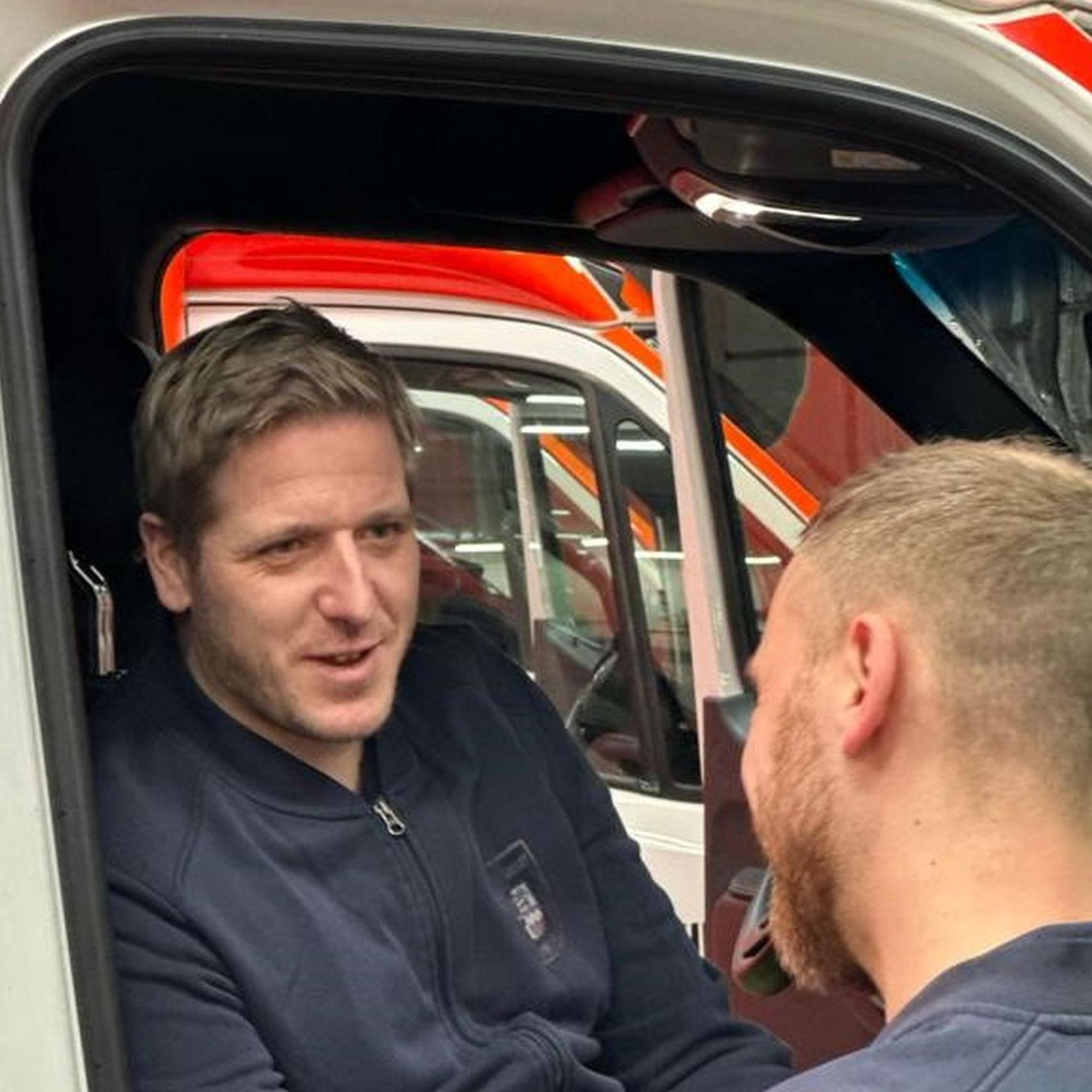 Landrat Markus Ramers sitzt auf dem Beifahrersitz eines Rettungswagens, die Tür ist geöffnet. Er unterhält sich mit seinem Rettungsdienstmitarbeiter.