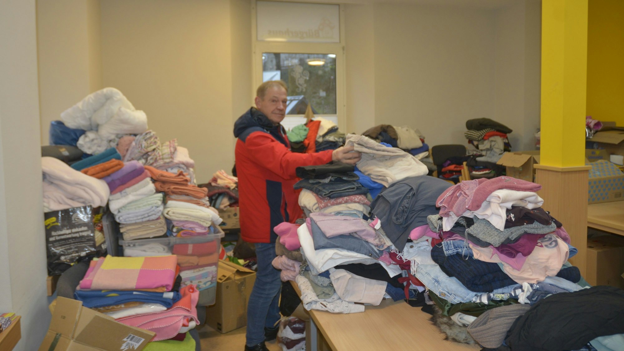 Dieter Leineweber steht zwischen Stapeln von Kleidung und zeigt, was alles abgegeben wurde.