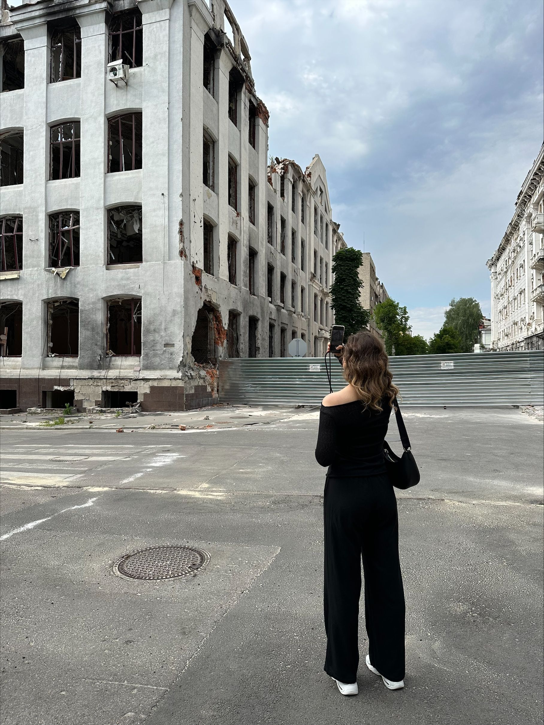 Eine Frau macht mit dem Handy ein Foto von einem zerstörten Haus.