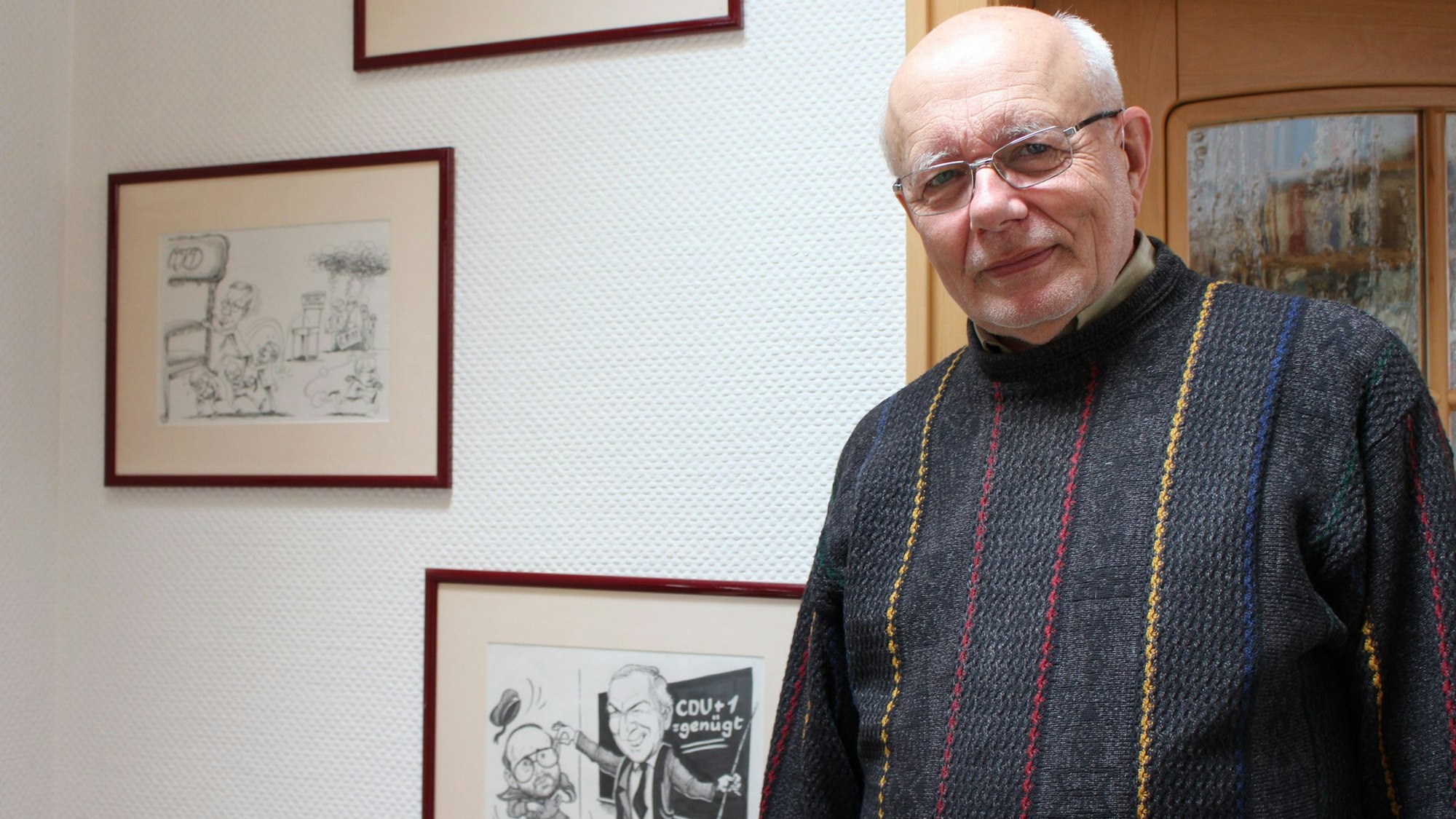 Hans Reiff steht vor einer Wand mit Karikaturen, auf denen er dargestellt wurde.