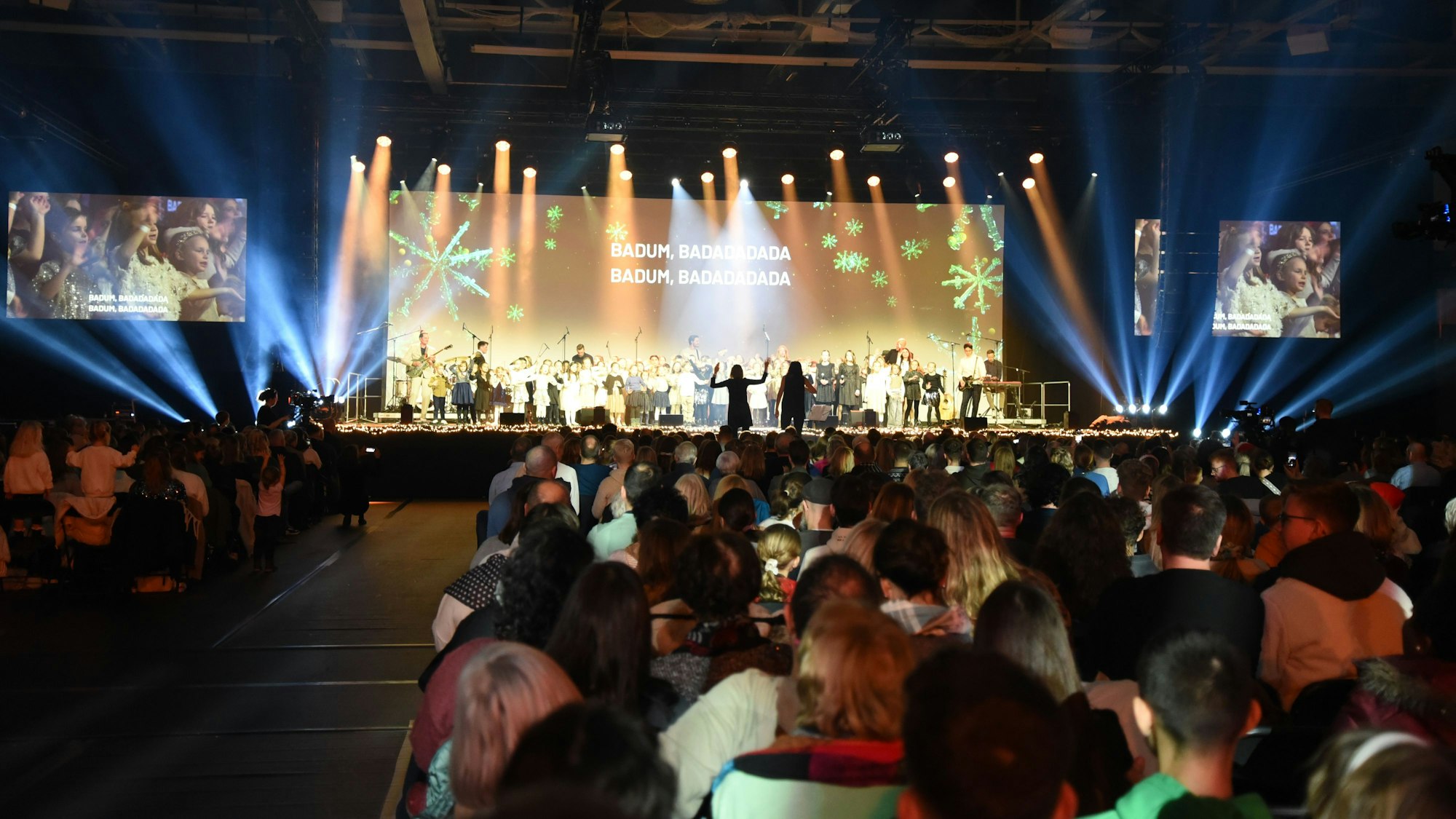 Blick in die volle Schwalbe-Arena. Auf der Bühne ist eine Leinwand, auf der Liedtexte von Weihnachtssongs angezeigt werden.