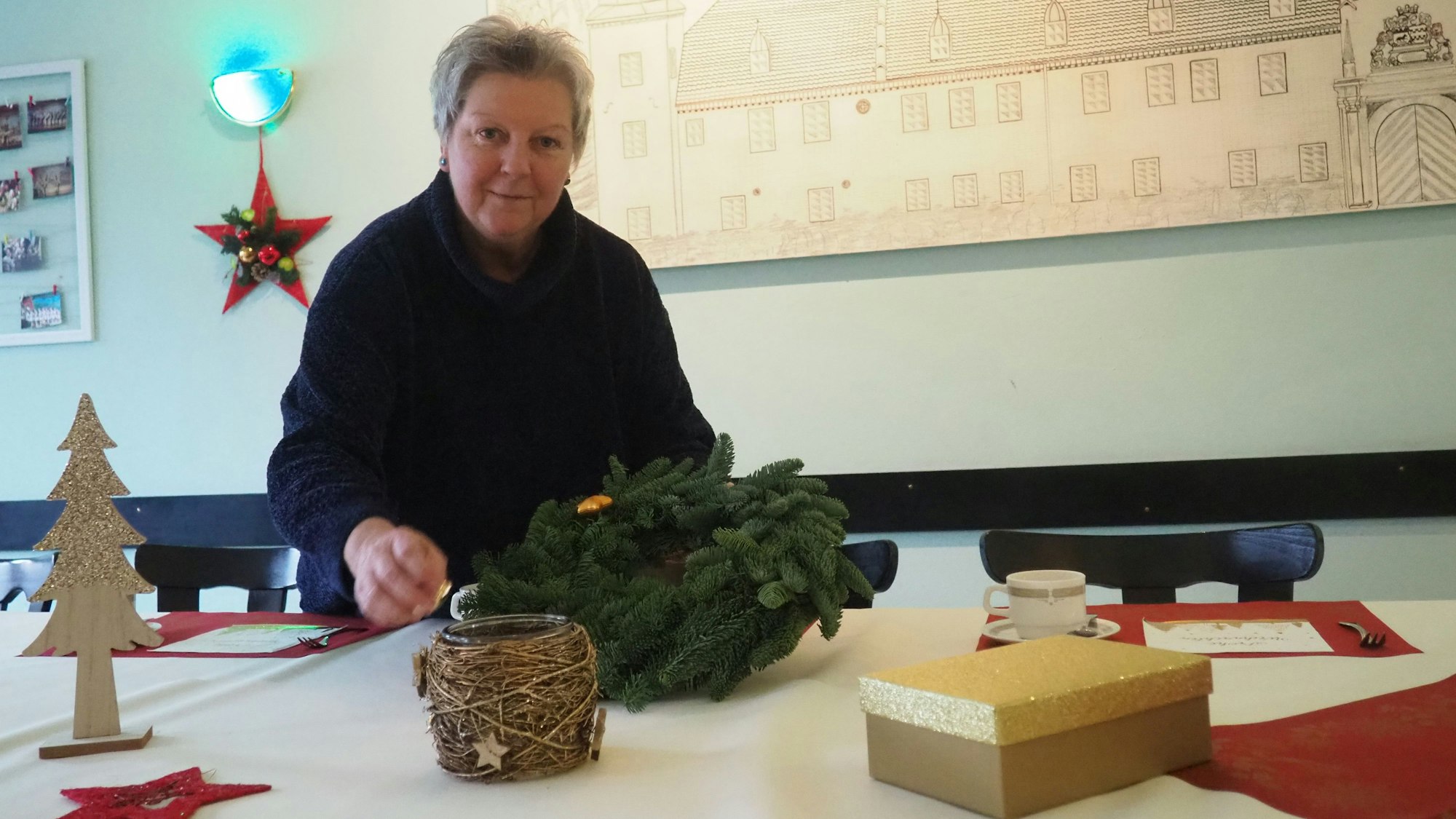 Eine Frau legt einen Adventskranz auf einen gedeckten Tisch.