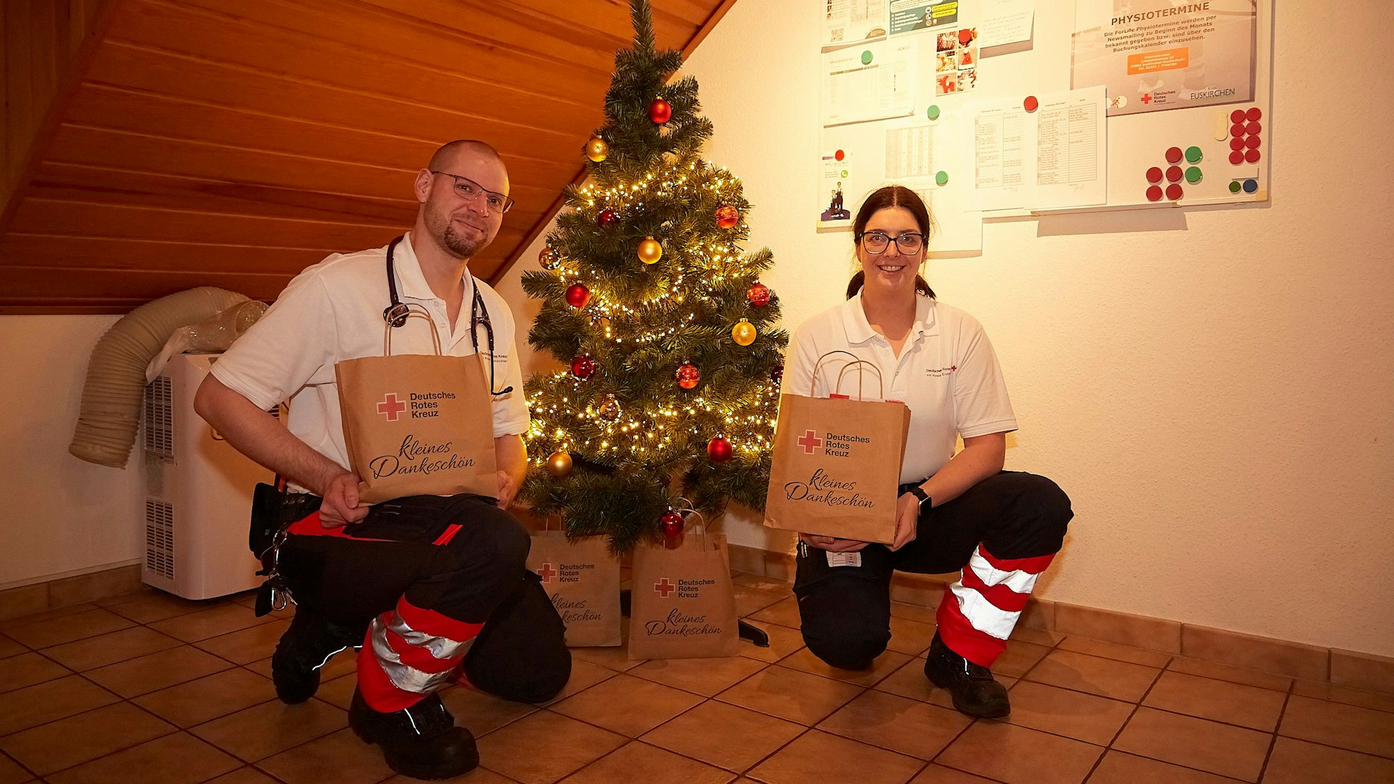 Matthias Unger und Vanessa Siebertz knien in der Rettungswache Tondorf an einem kleinen Weihnachtsbaum, mit dem sie ihre Unterkunft weihnachtlich geschmückt haben.