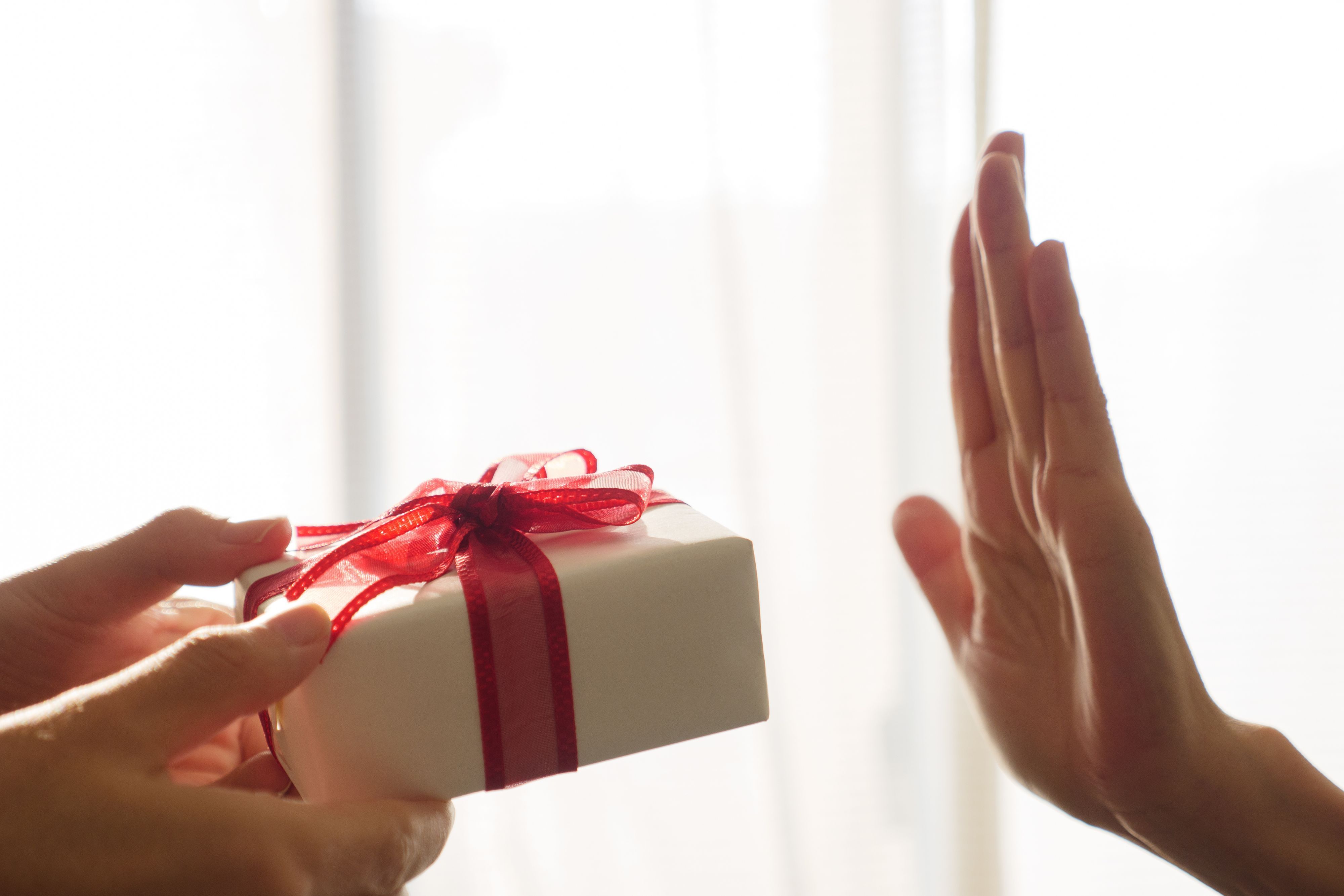 Zwei Hände halten ein Geschenkpäckchen, eine Hand ist abwehrend nach oben gereckt.