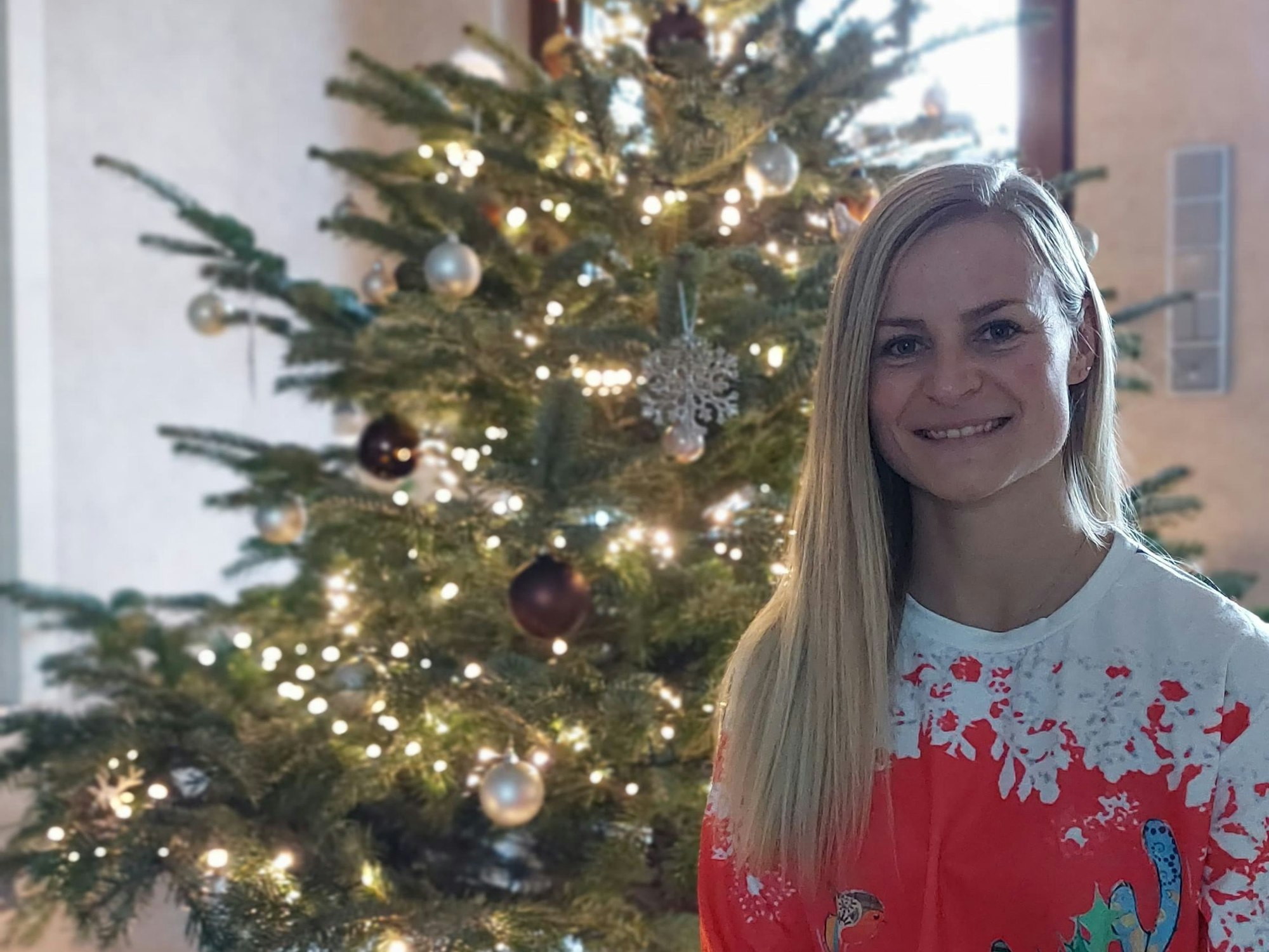 Jessica Rau sitzt in einem Weihnachtspulli vor einem geschmückten Tannebaum.