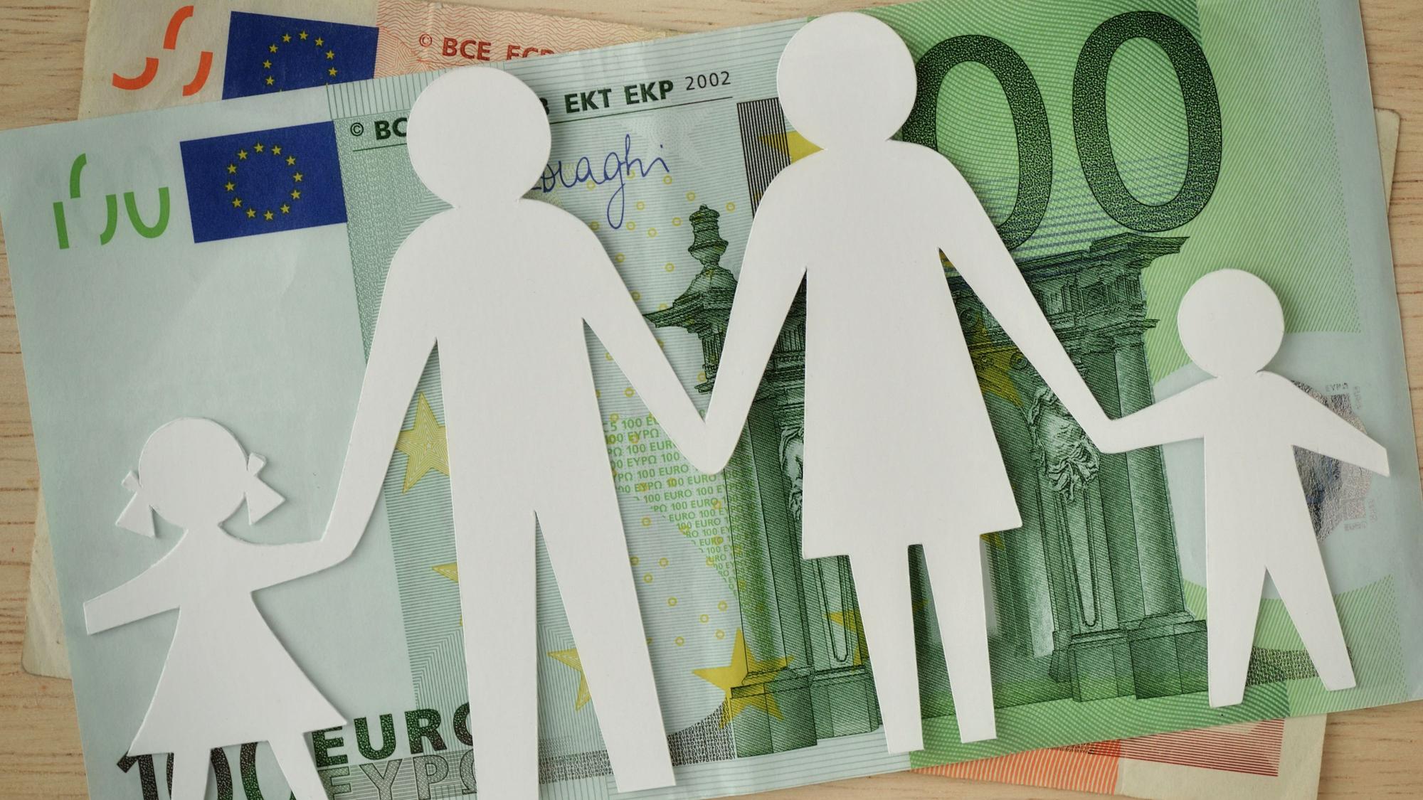 Eine Familie aus Papier ausgeschnitten liegt auf Geldscheinen.