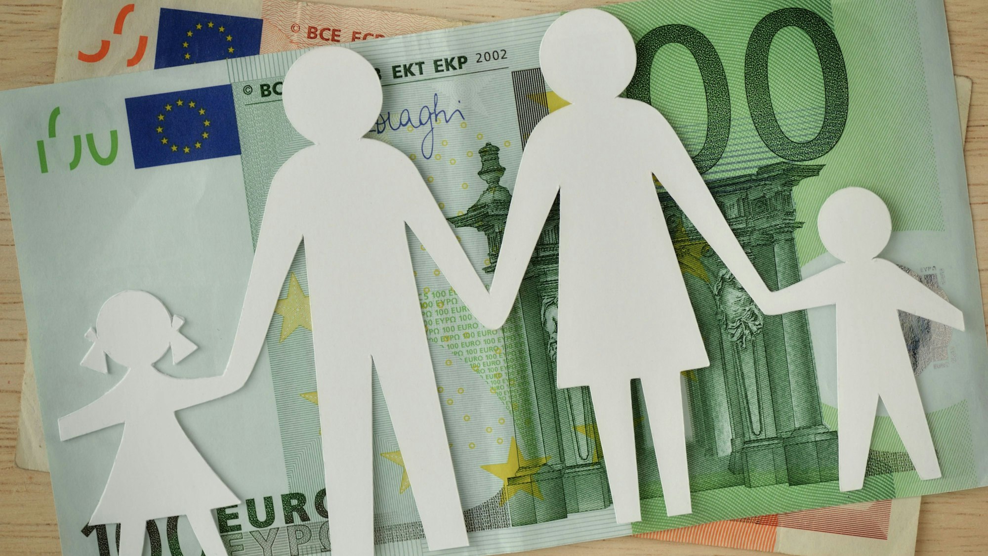 Eine Familie aus Papier ausgeschnitten liegt auf Geldscheinen.