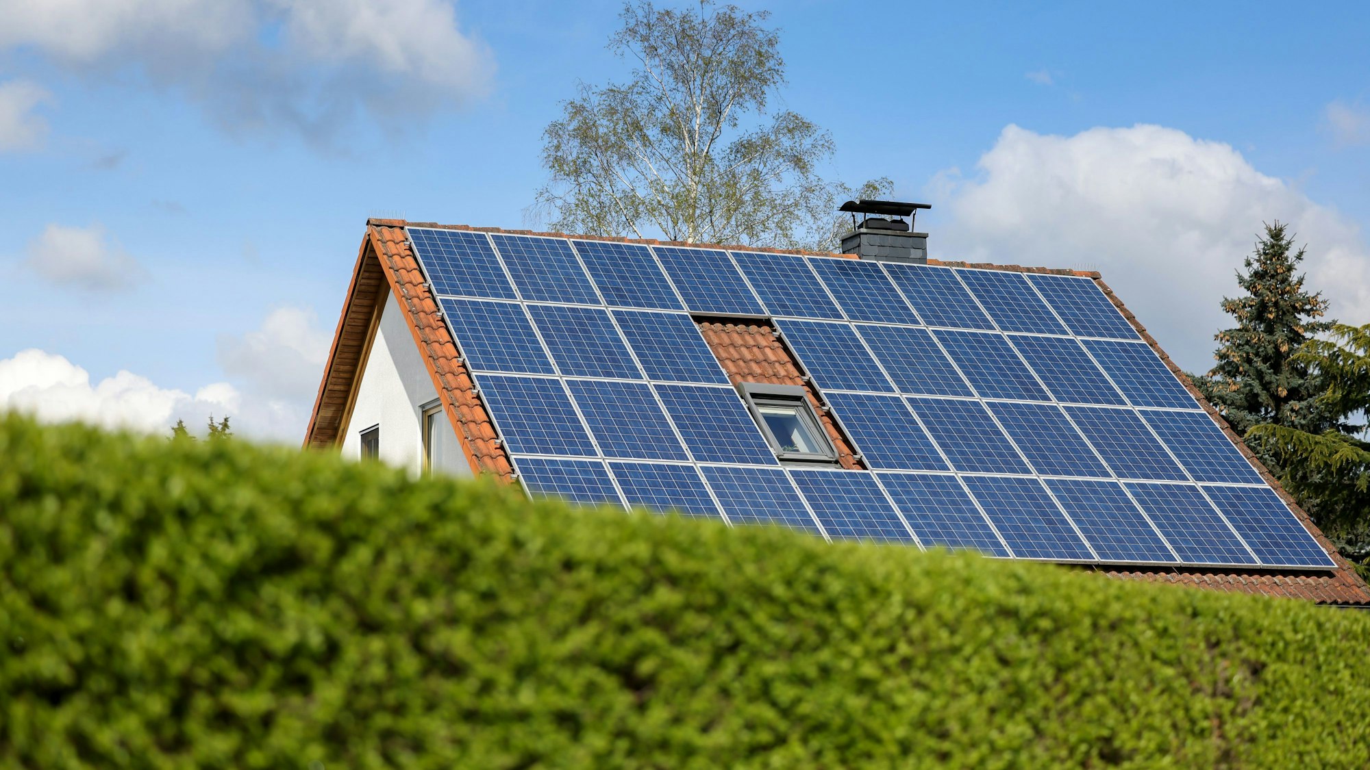 Haus mit Photovoltaik auf dem Dach hinter einer grünen Hecke.