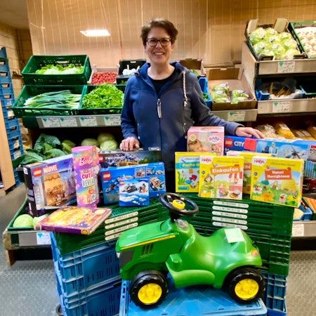 Zu sehen ist eine Frau mit vielen Geschenken, darunter ein grünes Bobby Car.