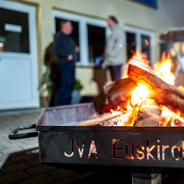 Das Bild zeigt eine Feuerschale in der JVA. Im Hintergrund stehen zwei Männer und unterhalten sich.