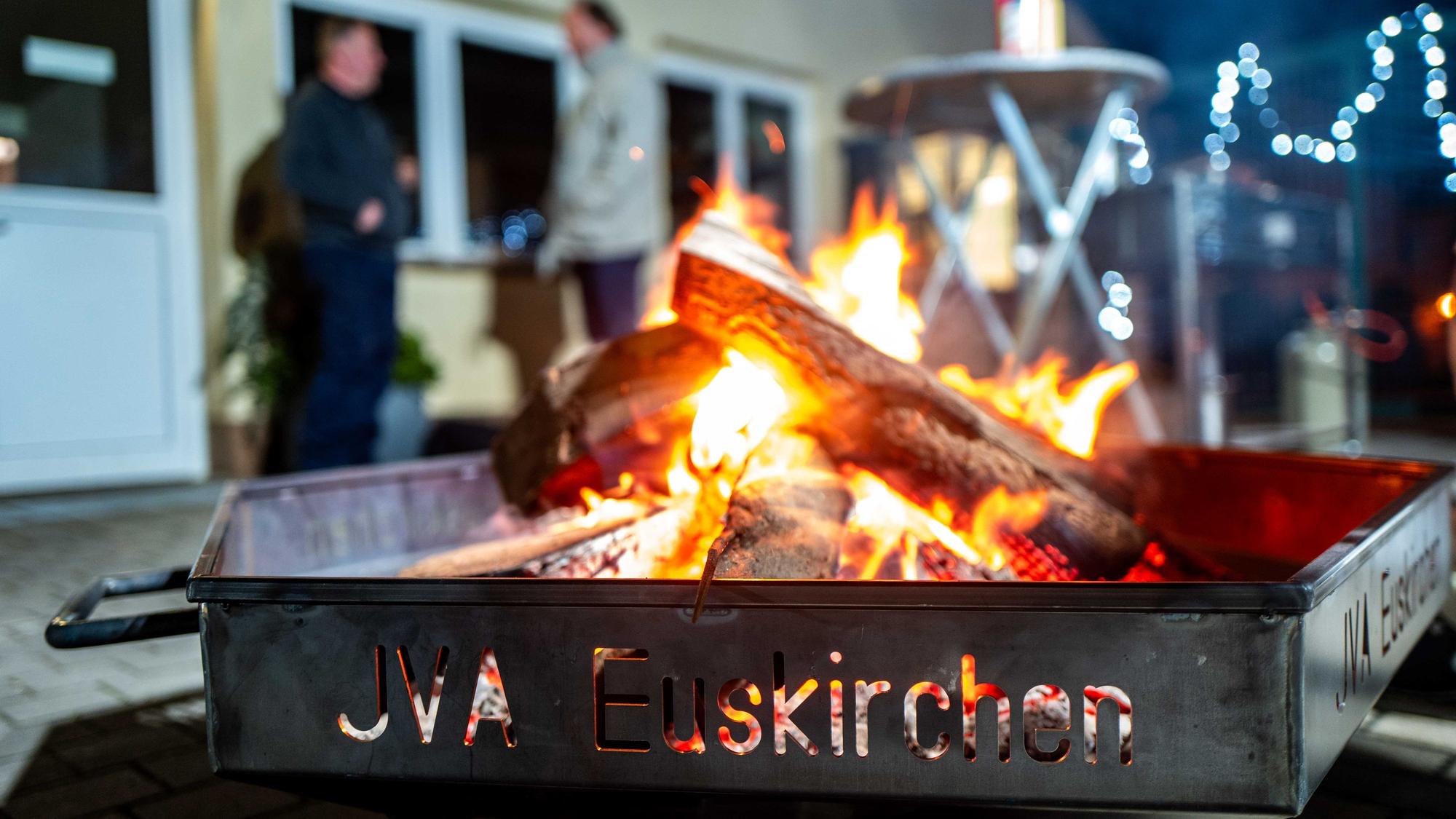 Das Bild zeigt eine Feuerschale in der JVA. Im Hintergrund stehen zwei Männer und unterhalten sich.