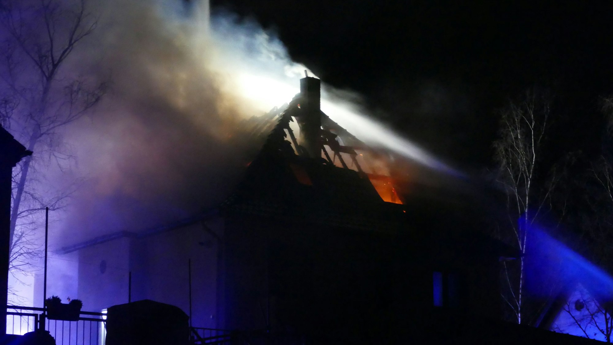 Eine Drehleiter der Feuerwehr steht vor einem brennenden Haus.