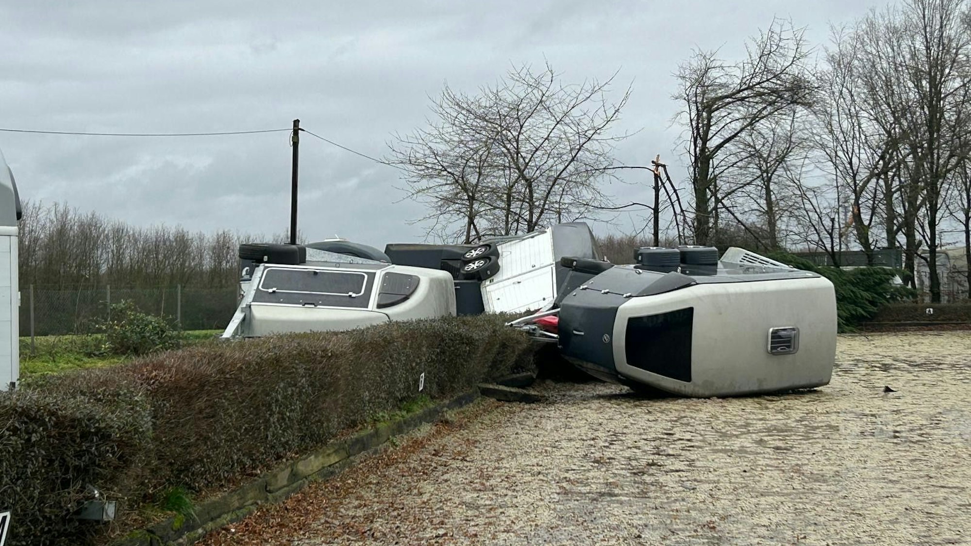 Pferdeanhänger liegen übereinander geworfen auf einem Sandplatz und teilweise in einer Hecke.