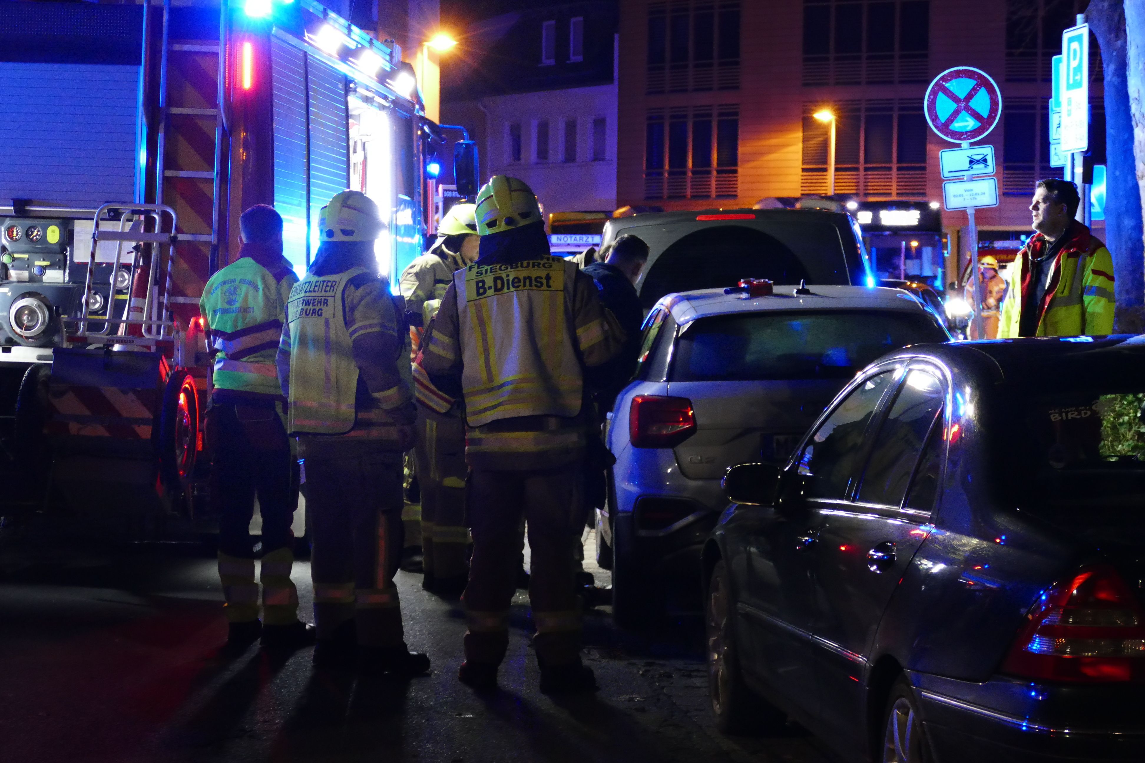 Rettungskräfte und ein Feuerwehrfahrzeug stehen in einer Straße mit parkenden Fahrzeugen.