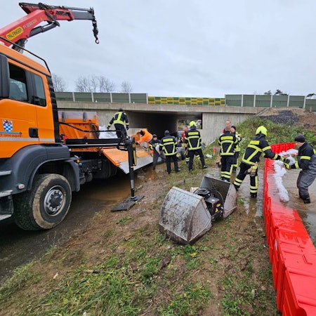 Feuerwehrleute legen Sandsäcke auf eine mobile Wand aus Plastik.