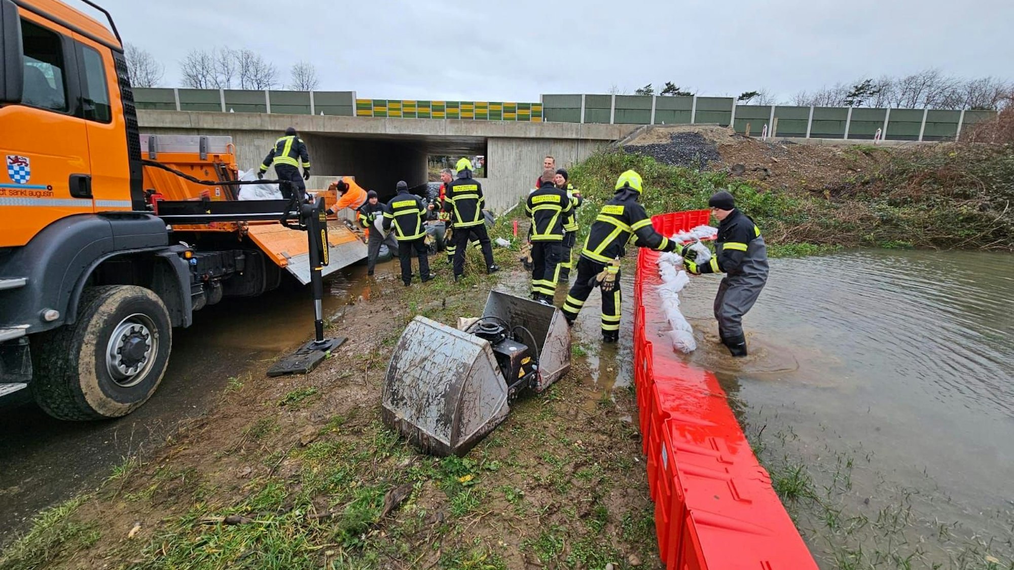 Feuerwehrleute legen Sandsäcke auf eine mobile Wand aus Plastik.