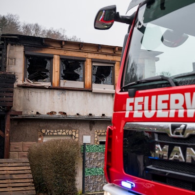 Ein Einsatzwagen der Feuerwehr steht vor einem Haus, das abgebrannt ist.