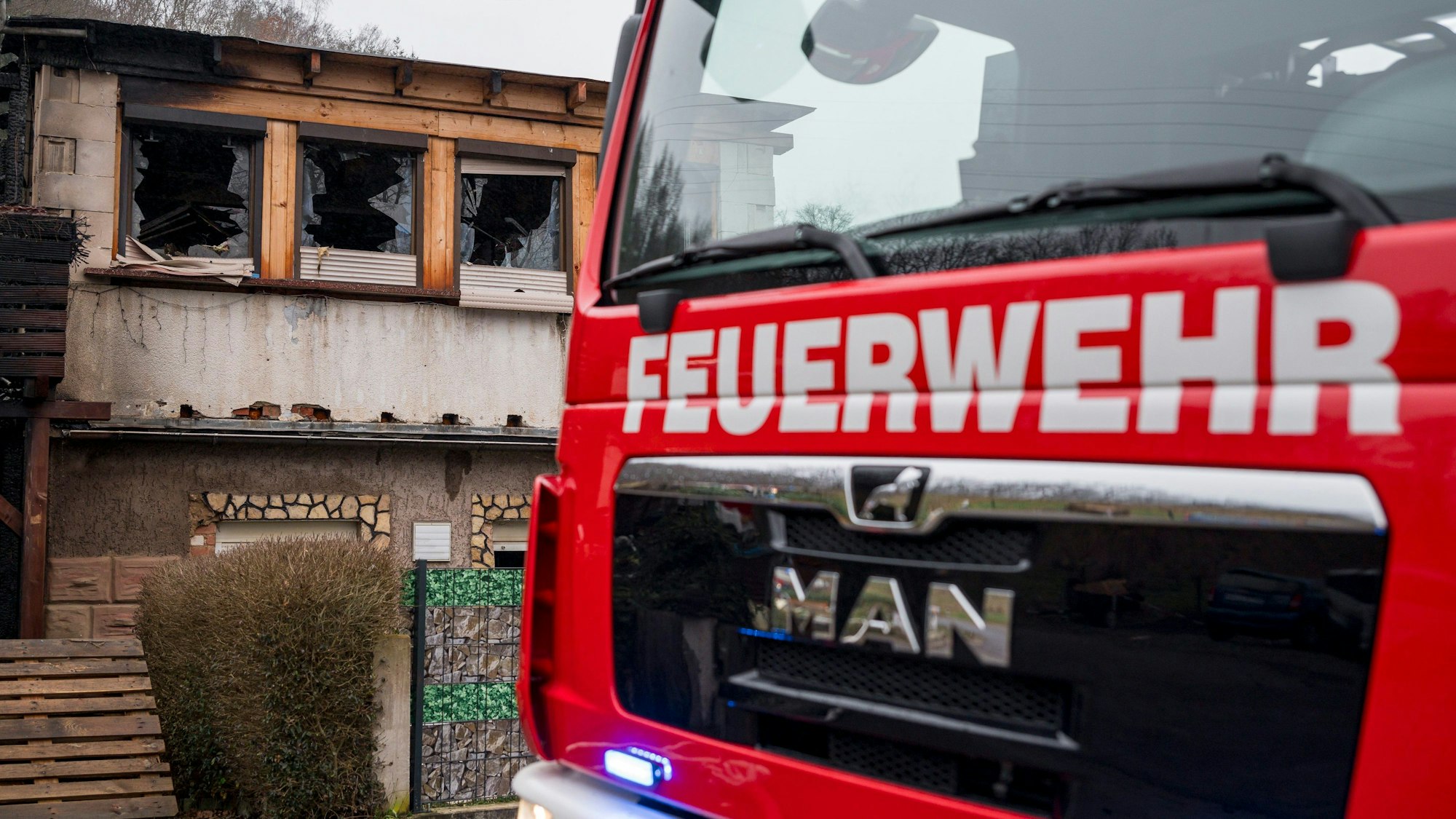 Ein Einsatzwagen der Feuerwehr steht vor einem Haus, das abgebrannt ist.