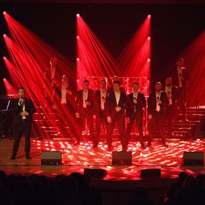 The 12 Tenors stehen auf der Bühne und werden von rot angestrahlt.
