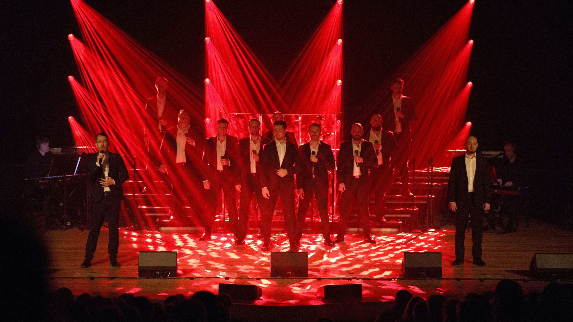 The 12 Tenors stehen auf der Bühne und werden von rot angestrahlt.