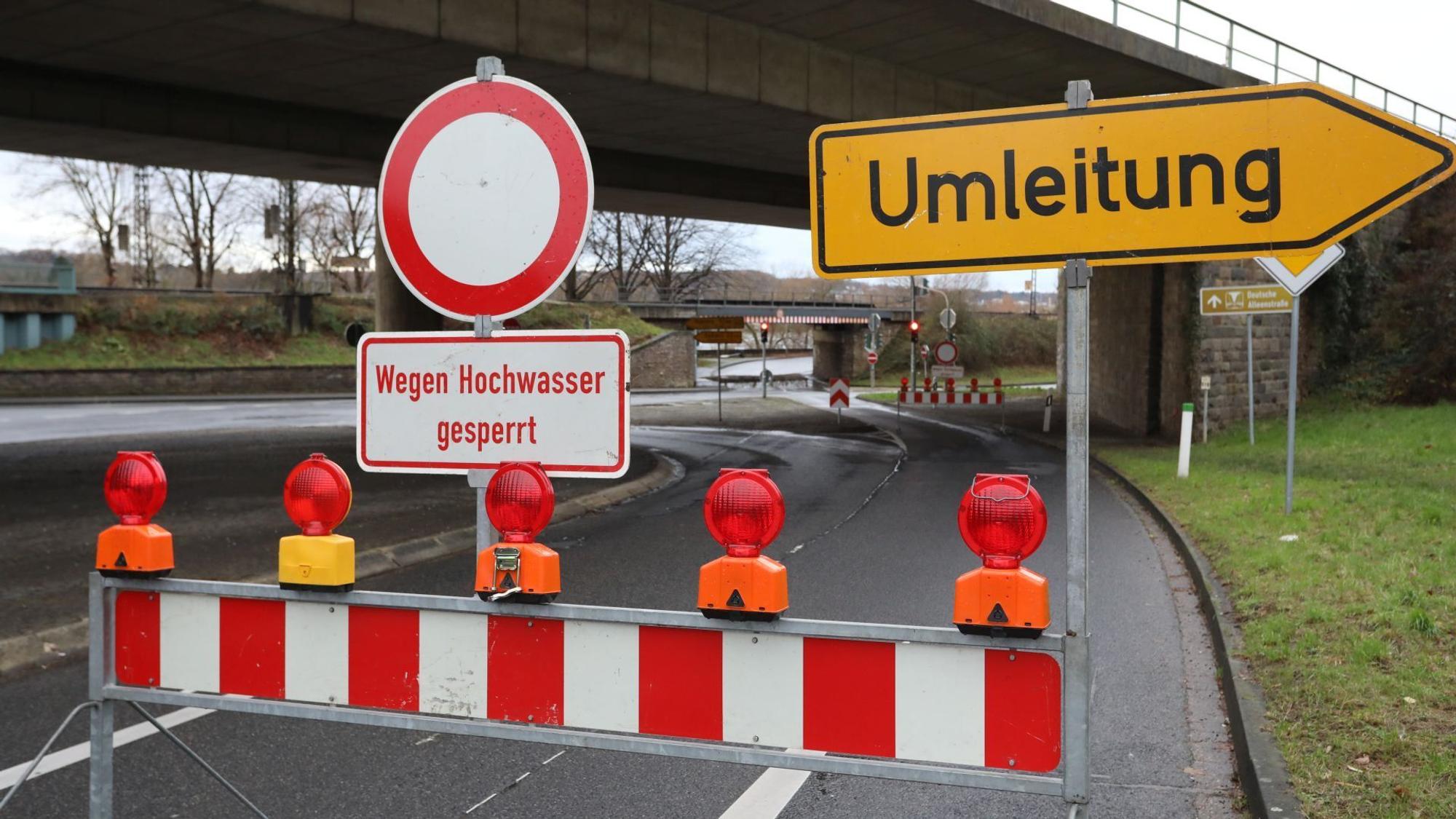 Eine rot-weiße Warnbake mit dem Hinweis auf das Hochwasser steht auf einer Straße.
