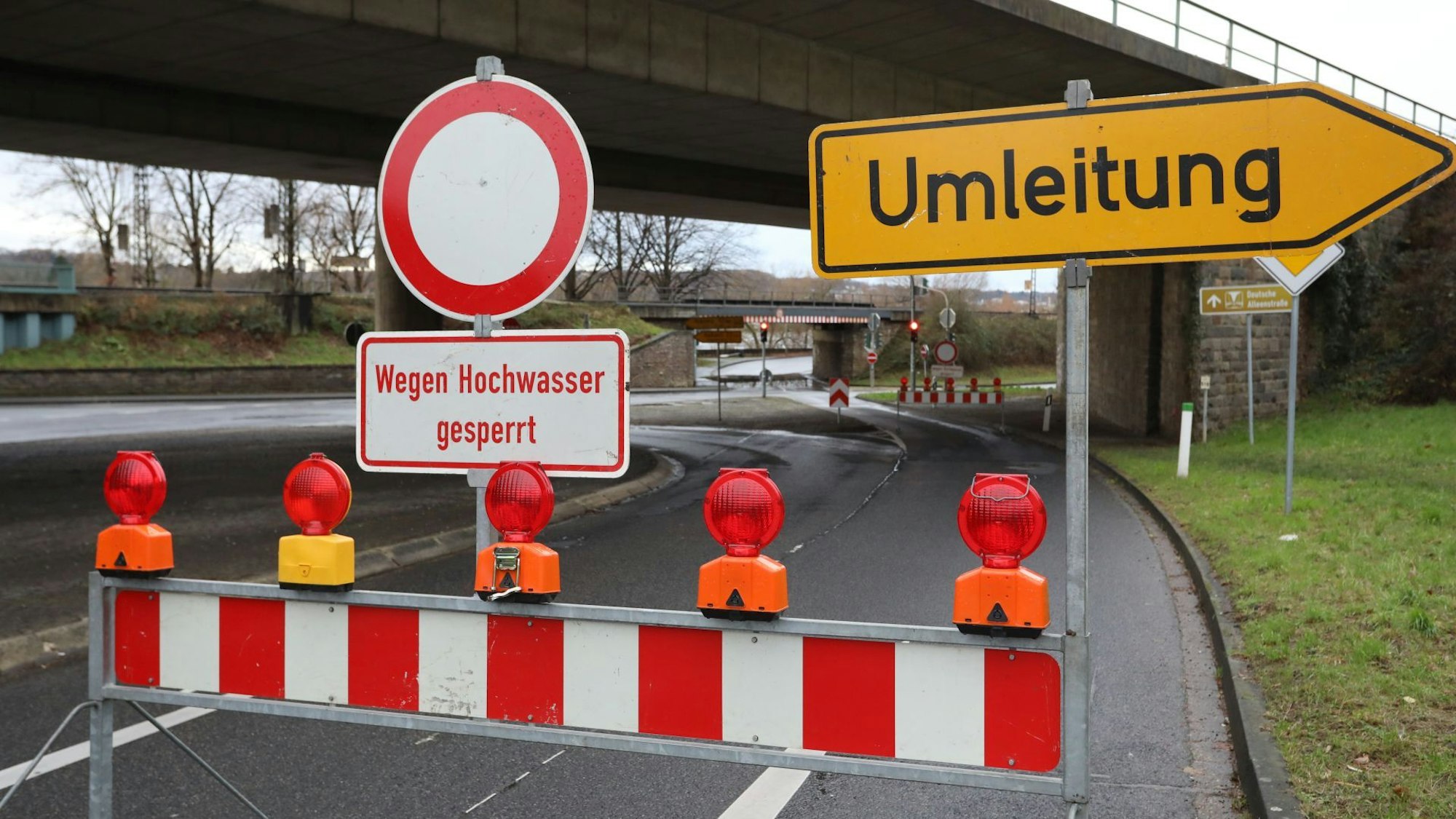 Eine rot-weiße Warnbake mit dem Hinweis auf das Hochwasser steht auf einer Straße.