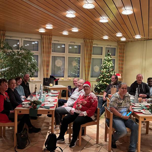 Menschen sitzen an gedeckten Tischen, im Hintergrund steht ein Weihnachtsbaum.