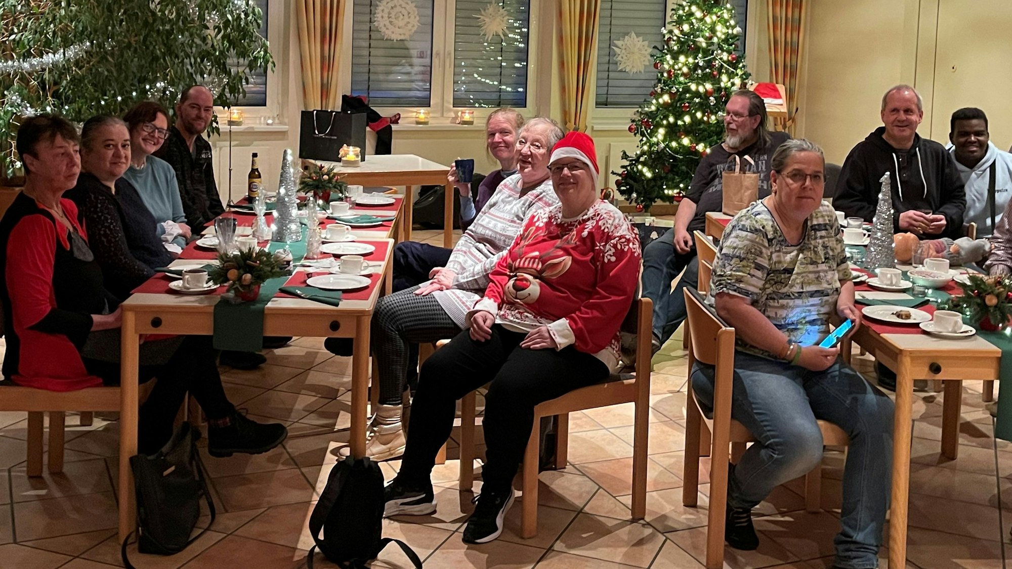 Menschen sitzen an gedeckten Tischen, im Hintergrund steht ein Weihnachtsbaum.