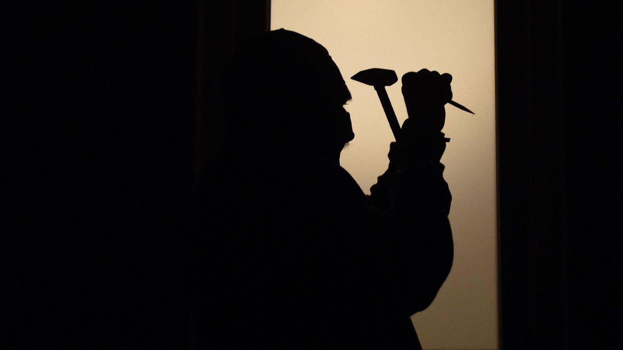 Ein Mann versucht mit einem Hammer und einem Schraubenzieher bei einem Einbruch ein Fenster aufzuhebeln