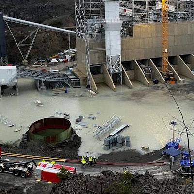 Ein Feuerwehrfahrzeug mit einem Abrollcontainer und Schläuchen steht neben einem gefluteten Steinbruch.