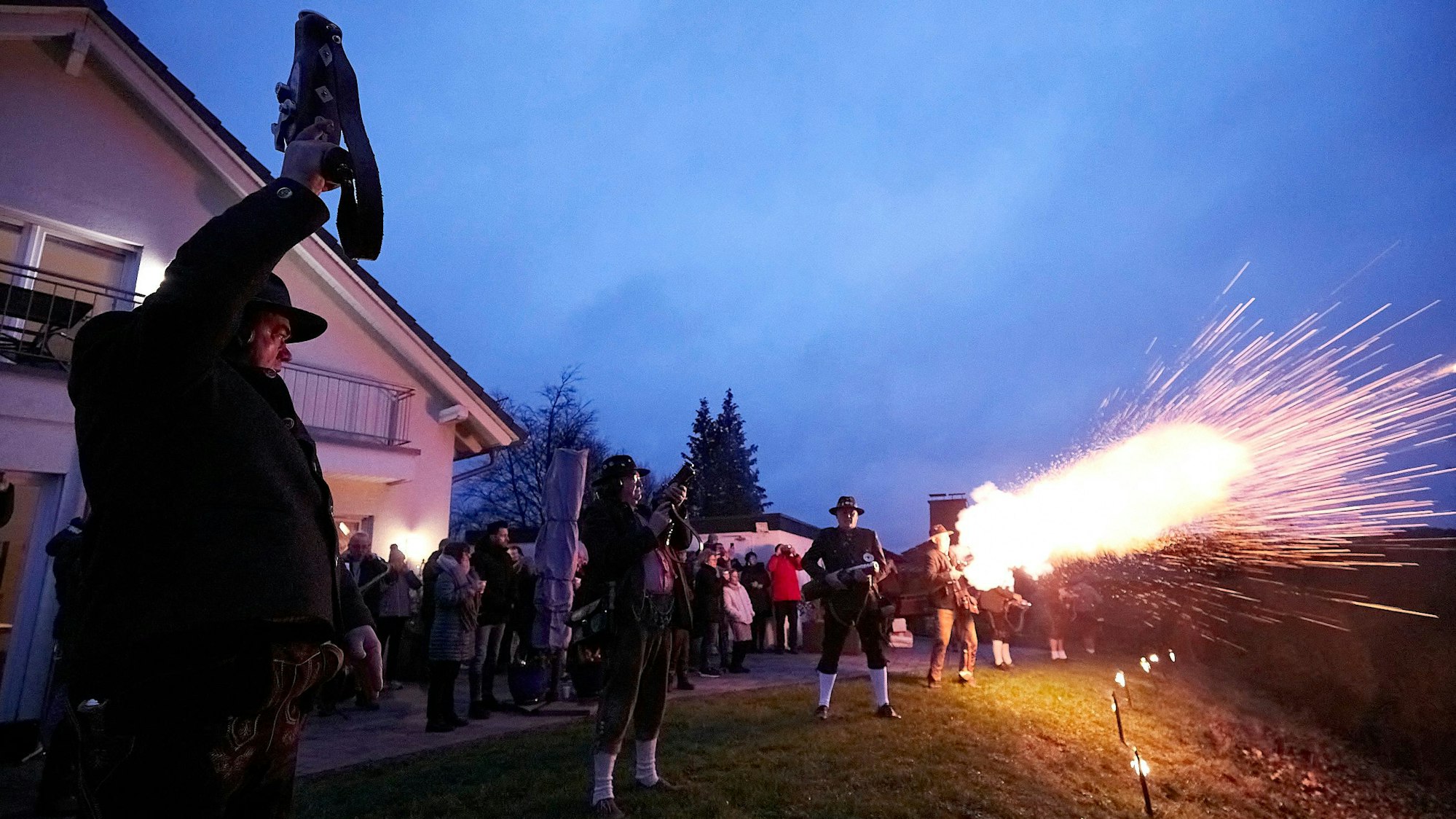 Ein Mann schießt in die Luft, man sieht einen Lichtschein und ein paar Männer, die Böller in die Luft schießen.