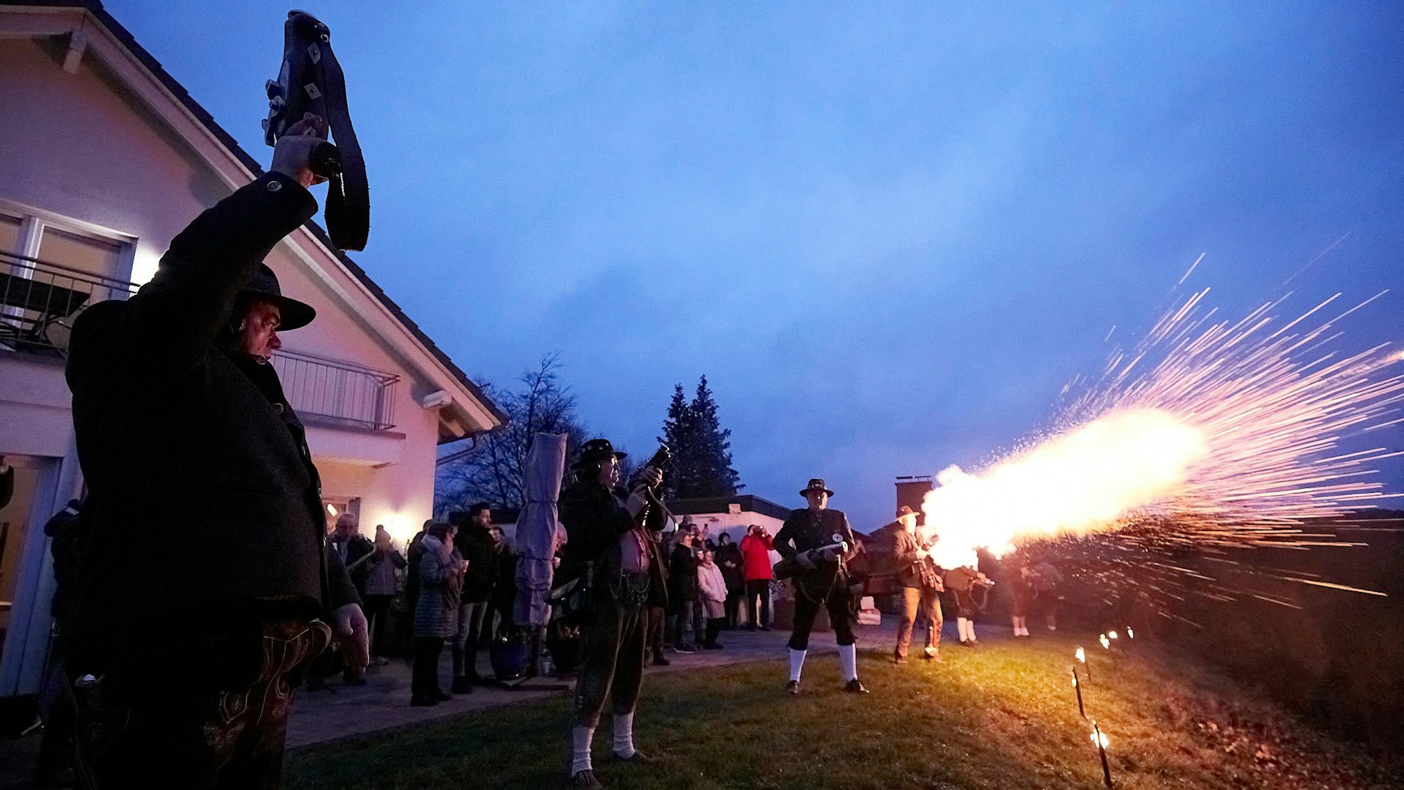 Ein Mann schießt in die Luft, man sieht einen Lichtschein und ein paar Männer, die Böller in die Luft schießen.