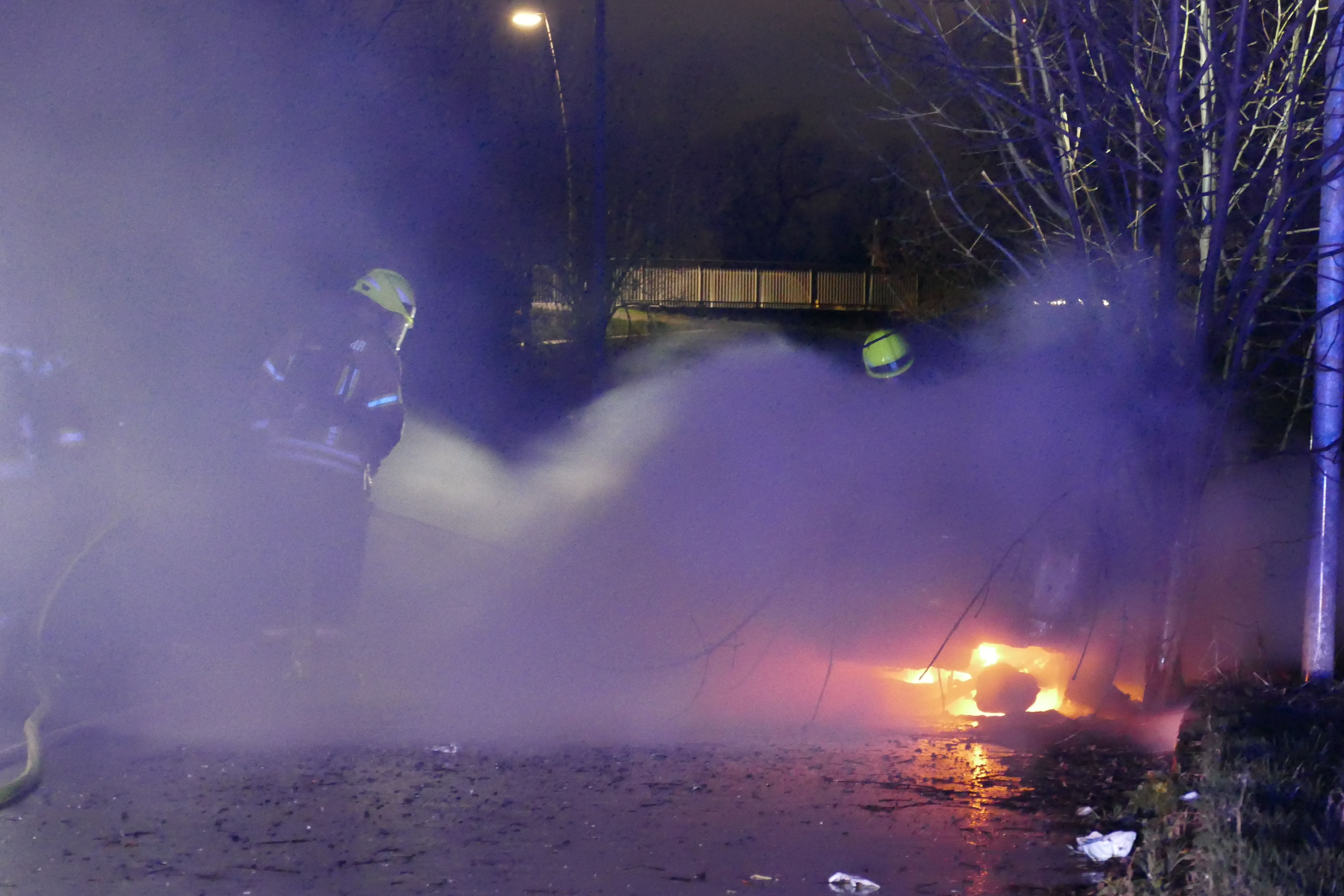 Feuerwehrleute stehen in dichtem Qualm und löschen, heller Flammenschein ist zu sehen.