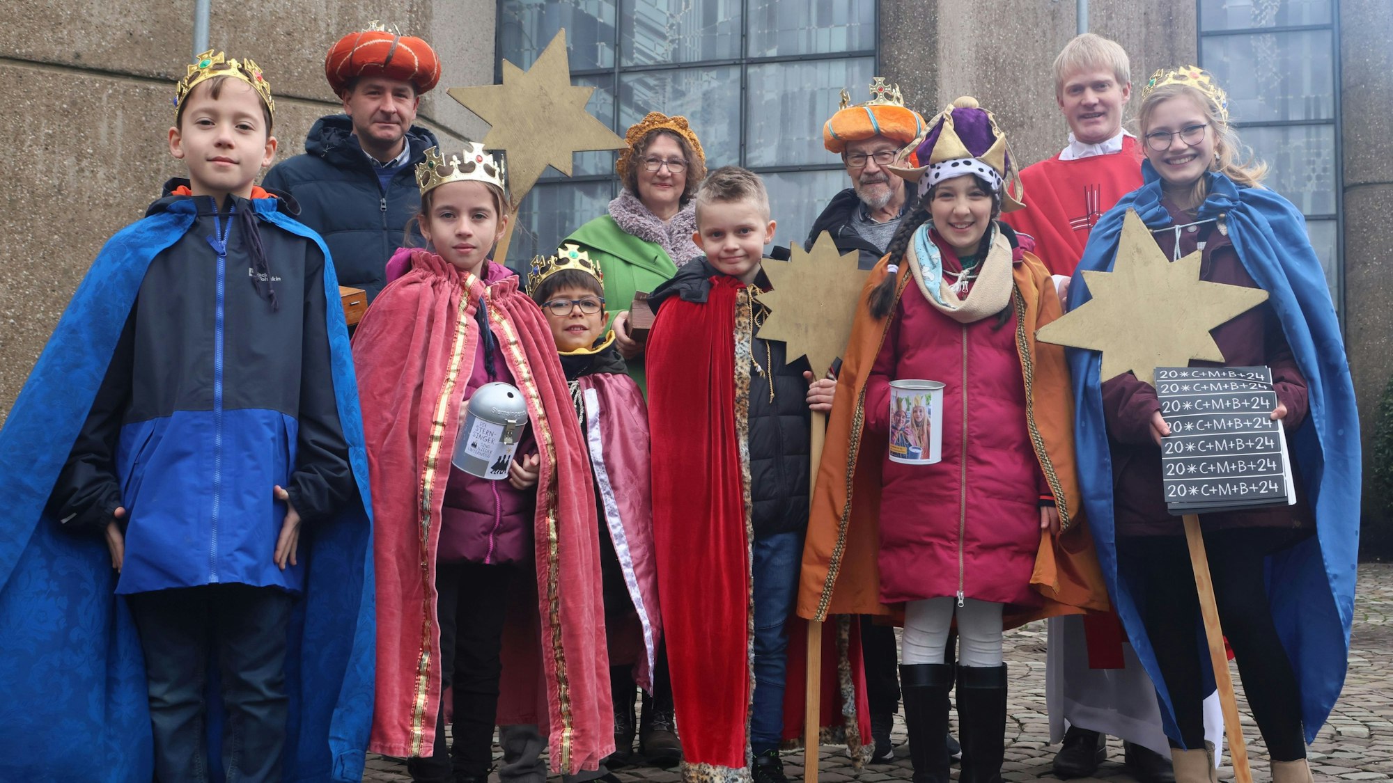 Eine Gruppe Sternsinger steht mit einem Kaplan zusammen vor einer Kirche.