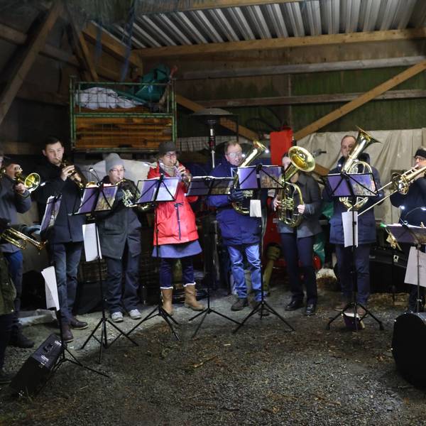 Ein Posaunenchor spielt in einer Remise eines landwirtschaftlichen Betriebs.
