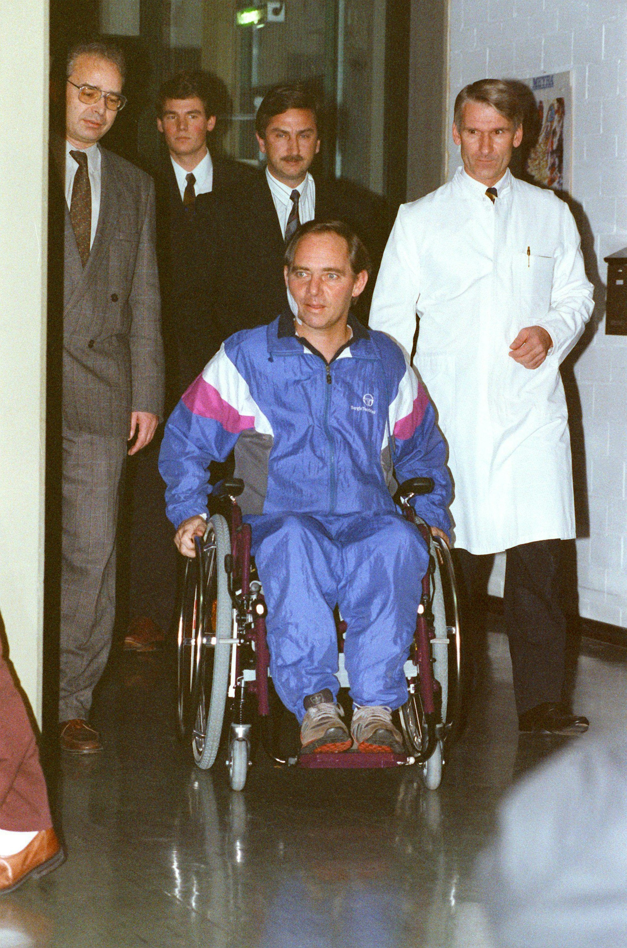 Karlsbad-Langensteinbach in Baden-Württemberg 1990: Knapp sechs Wochen nach dem Attentat begibt sich Wolfgang Schäuble (M, Rollstuhl) in der Rehabilitationsklinik zu seiner ersten Pressekonferenz. In seiner Begleitung Professor Jürgen Harms.