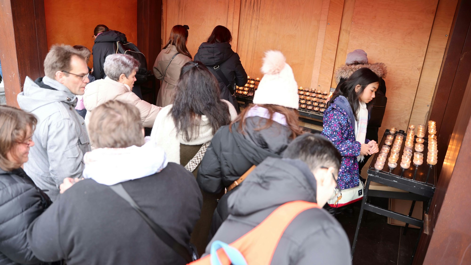 Menschen entzünden Kerzen in einer Weihnachtsmarktbude vor dem Dom.