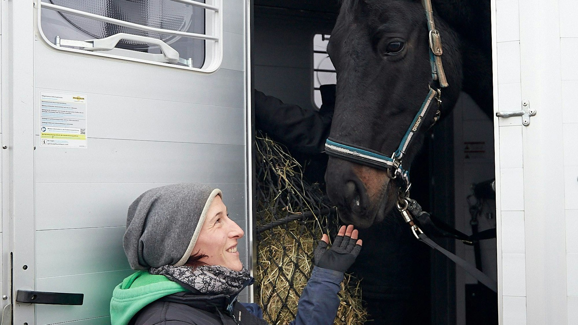 Nina Aschhoff steht an der Tür eines Transporters, in dem sich ein schwarzes Pferd befindet.