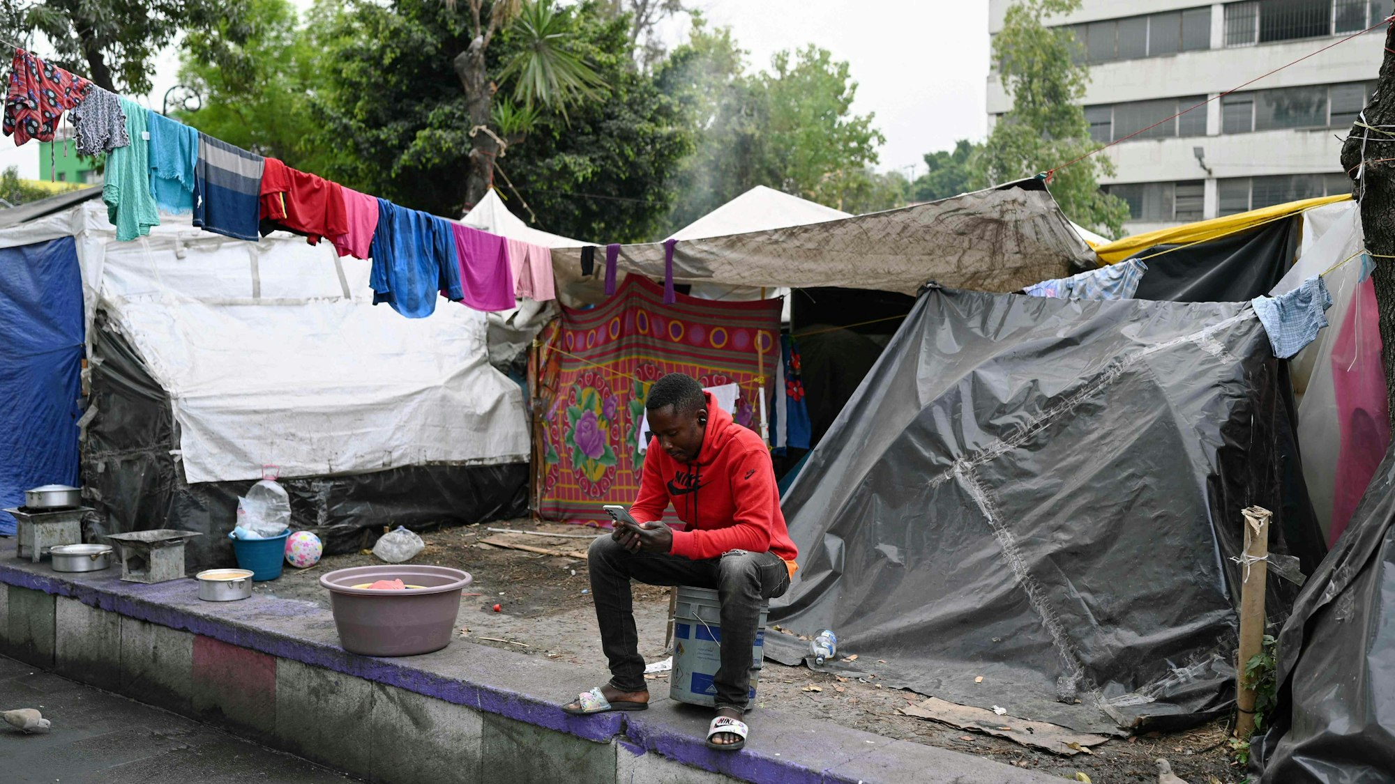 Ein Mann schaut in einem provisorischen Lager in Mexiko Stadt auf sein Handy.