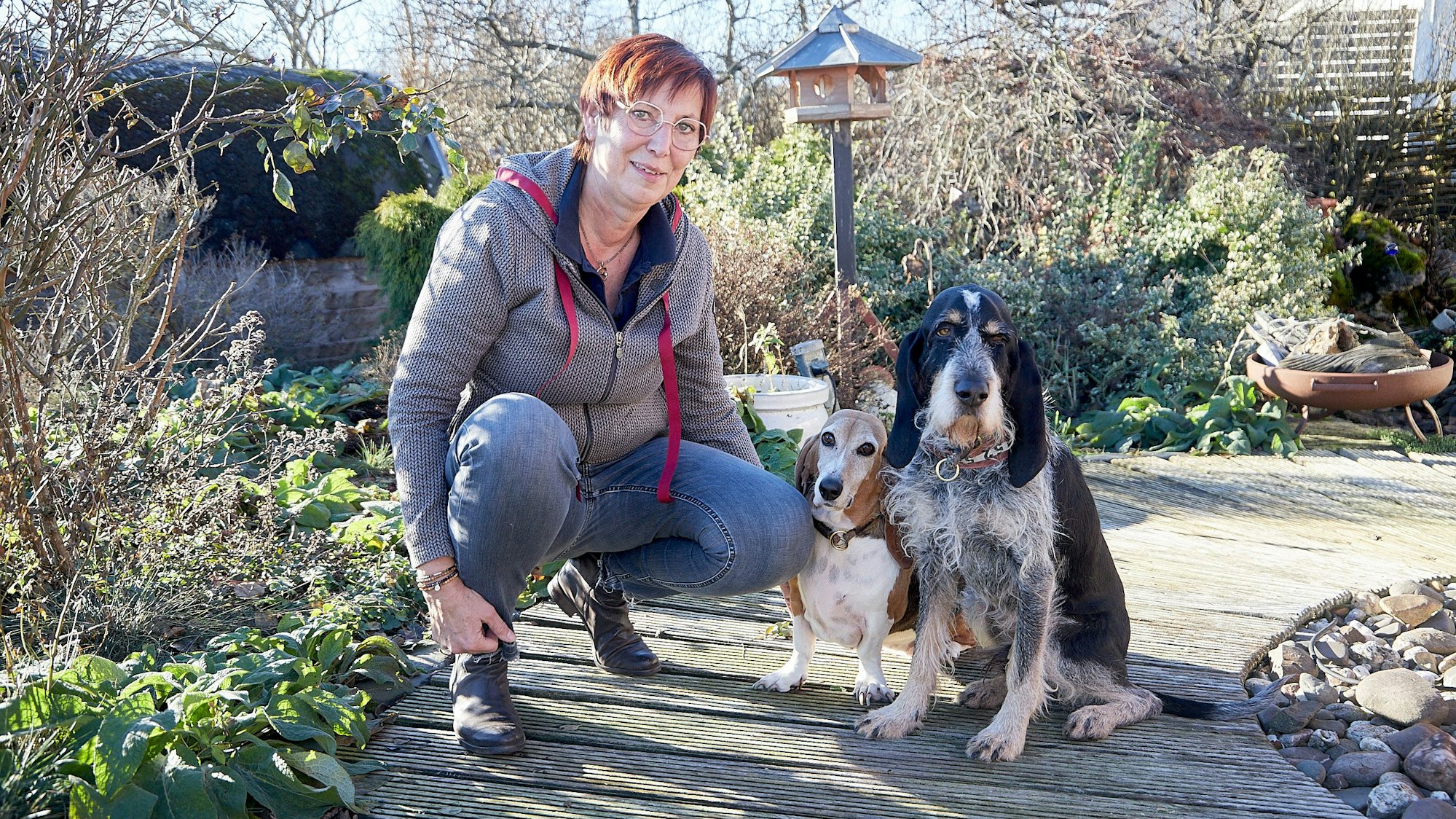 Franziska Weyer hockt in einem Garten neben zwei Hunden, einem Basset und einem Griffon.