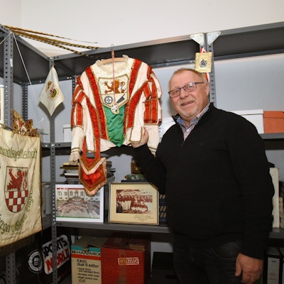 Ein Mann steht in einem Archiv im Keller vor vielen Karnevalsrelikten.