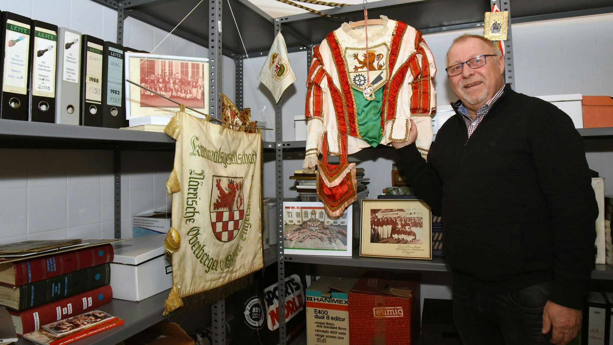 Ein Mann steht in einem Archiv im Keller vor vielen Karnevalsrelikten.