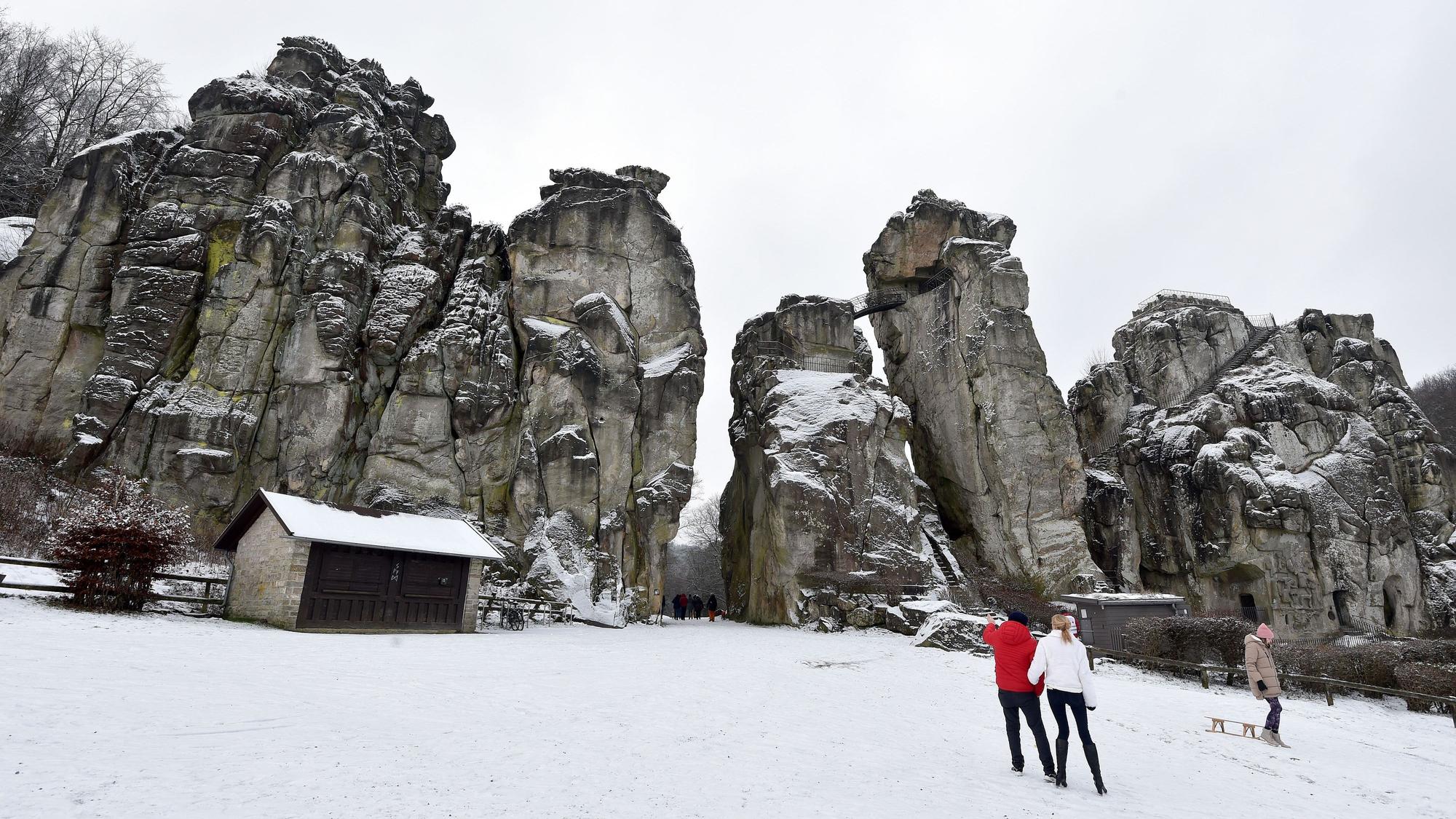 Spaziergänger stehen vor den schneebedeckten Externsteinen