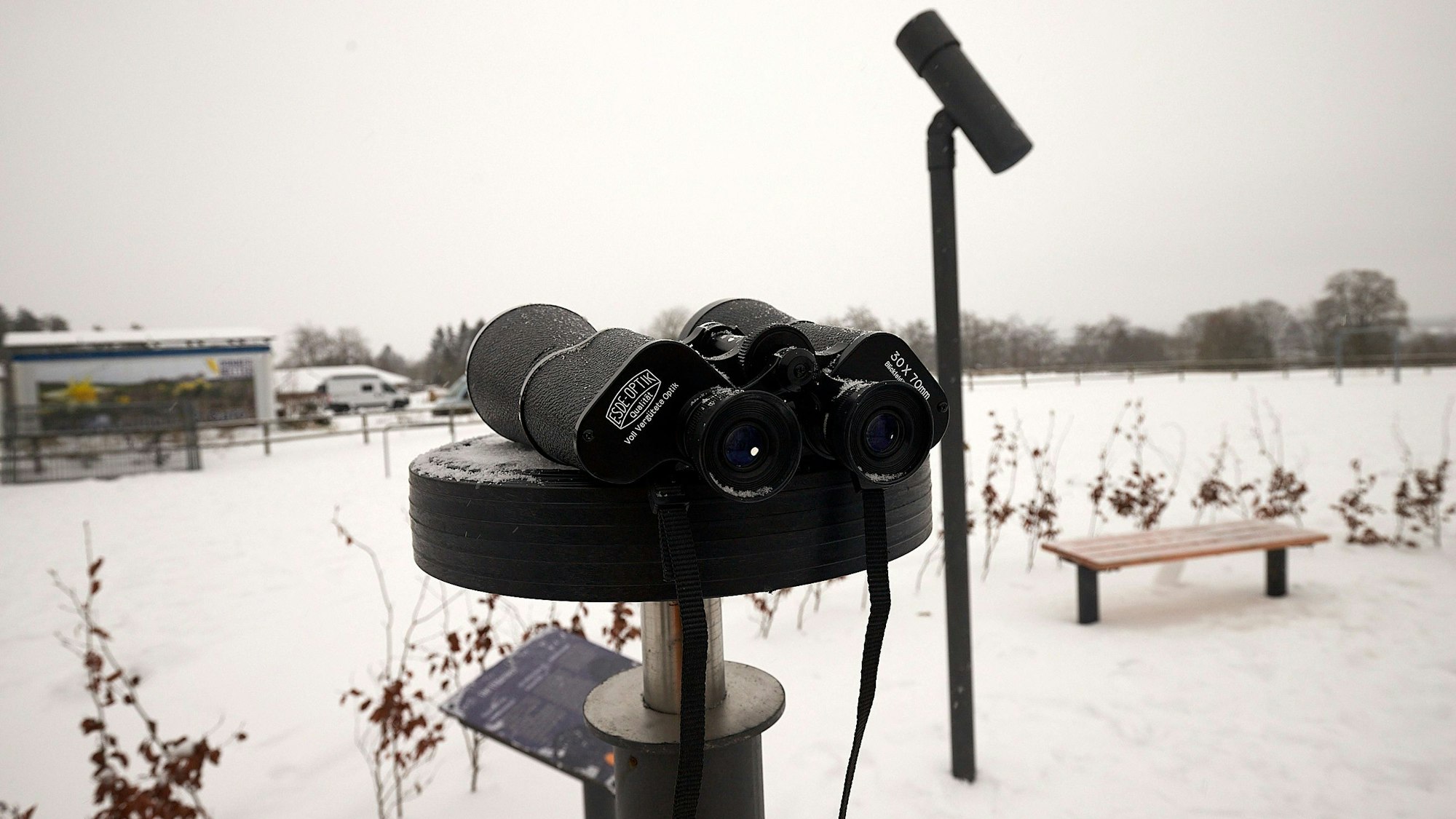 Ein Fernglas liegt auf einer Stützvorrichtung, dahinter ein senkrechter Pfosten mit dem in den Himmel gerichteten Zielrohr.