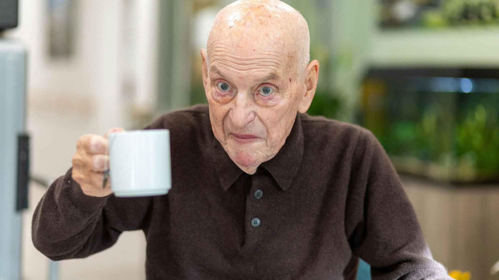 Das Foto zeigt einen Gast des Hospizes, der eine Tasse in die Kamera hält.