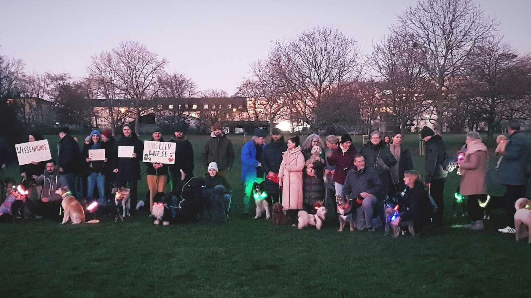 Herrchen und Hunde stehen mit Protestschildern im Park.
