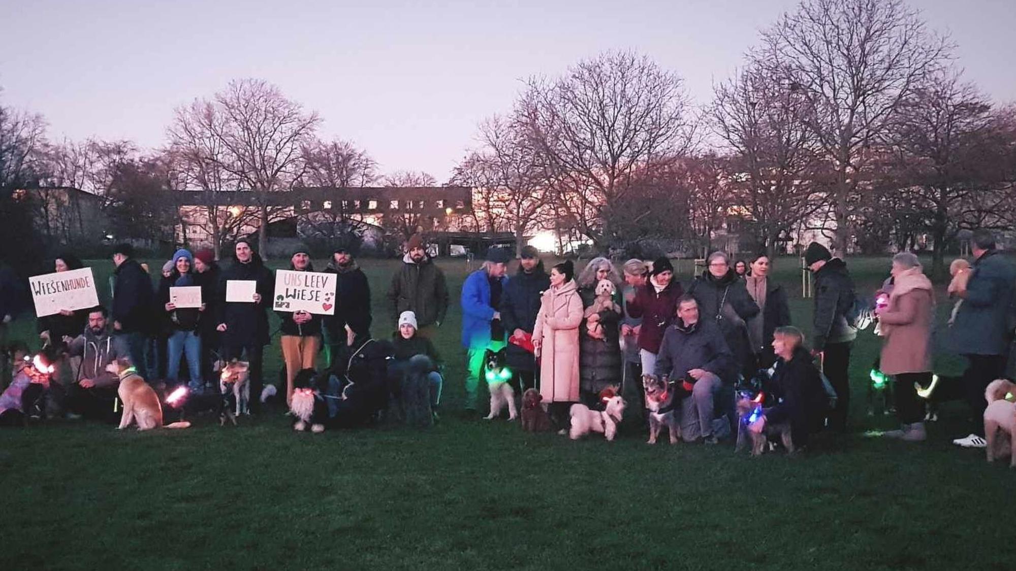 Herrchen und Hunde stehen mit Protestschildern im Park.