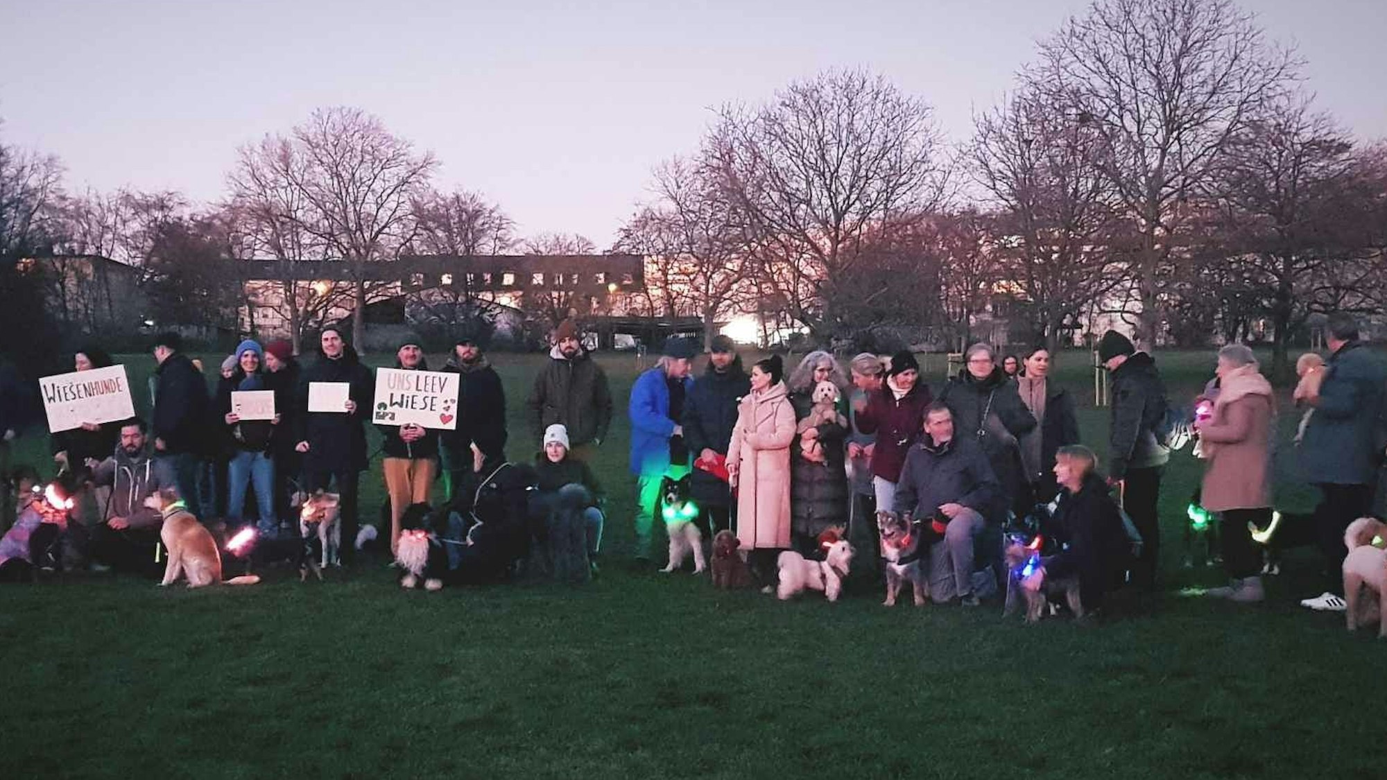 Herrchen und Hunde stehen mit Protestschildern im Park.