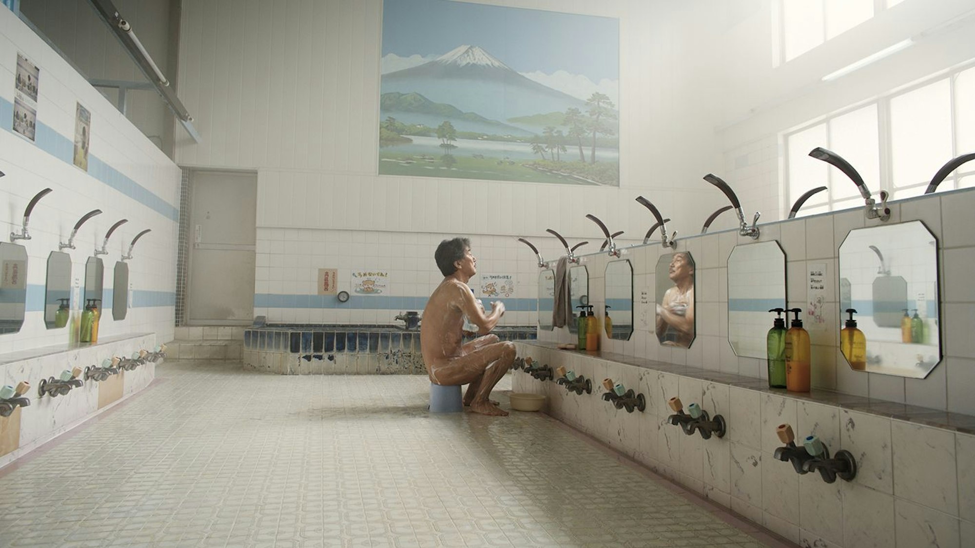 Ein Mann sitzt nackt in einem Badehaus vor einem Spiegel.